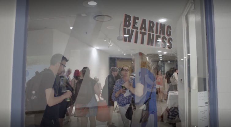 People seen looking through a glass window under the words 'bearing witness.'