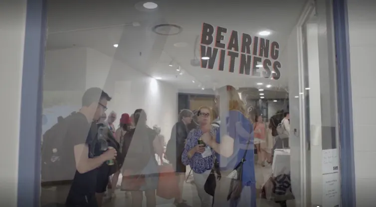 People seen looking through a glass window under the words 'bearing witness.'