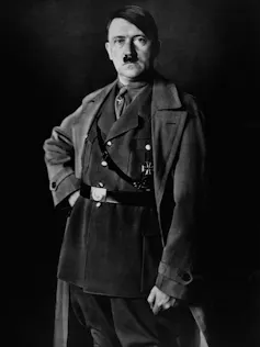 A white man with a little mustache poses while wearing a military uniform and overcoat.