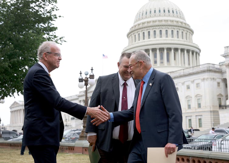 Two men in suits shake hands in front of the US Capitol.