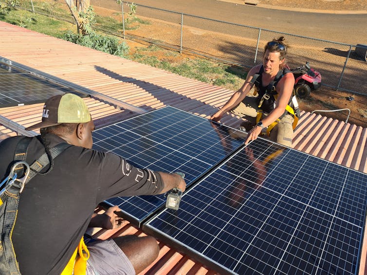 Two workers install solar panels on a rooftop