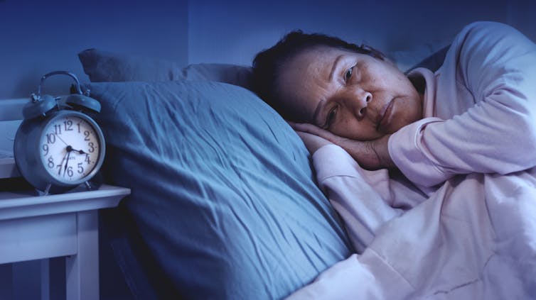 Older Asian woman awake in bed, alarm clock at about 3.30am