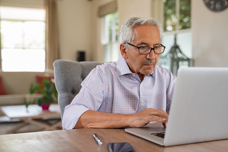 Older man on laptop, at desk, at home