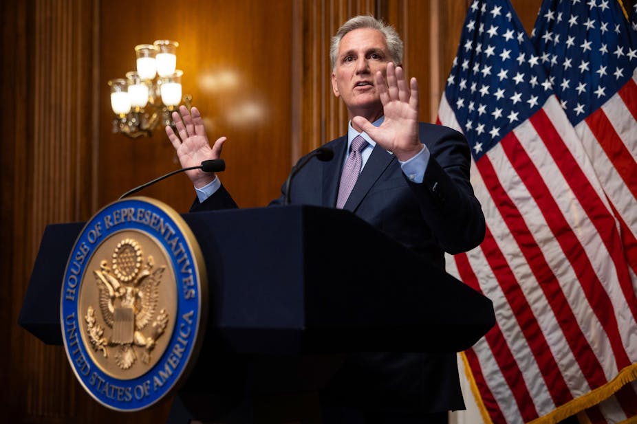 Republican Kevin McCarthy  holds his hands up as he stands at a podium.