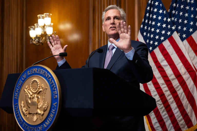 Republican Kevin McCarthy holds his hands up as he stands at a podium.
