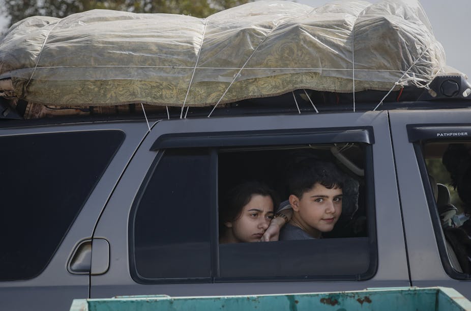 Two children stare out of the windown of a car with all their family's possessions on the roofrack.