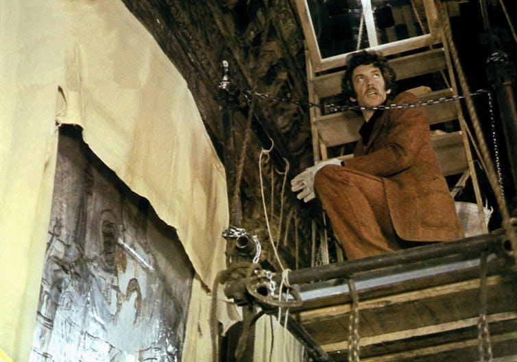 A man perched on some scaffolding in the roof space of an ancient church in Venice.