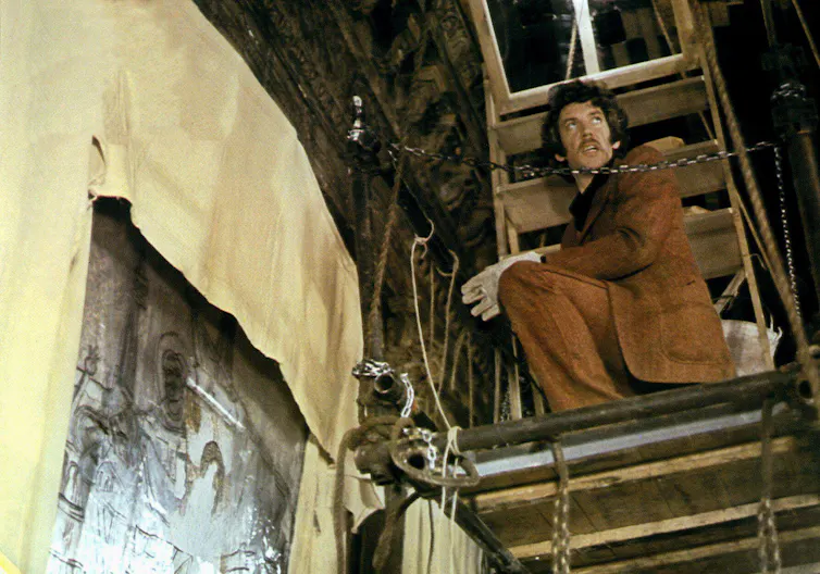 A man perched on some scaffolding in the roof space of an ancient church in Venice.