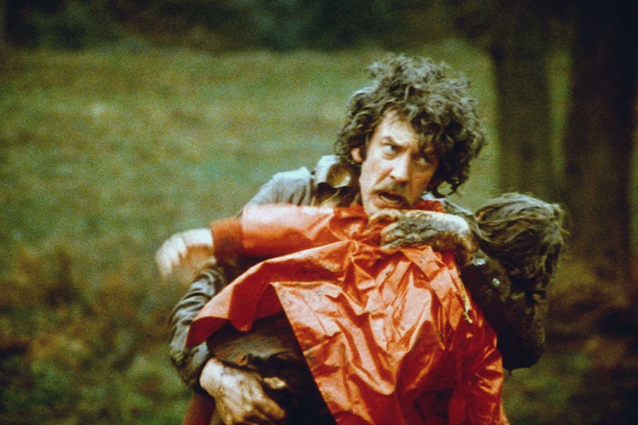 A distressed man holding his drowned daughter who is dressed in a bright red mac.