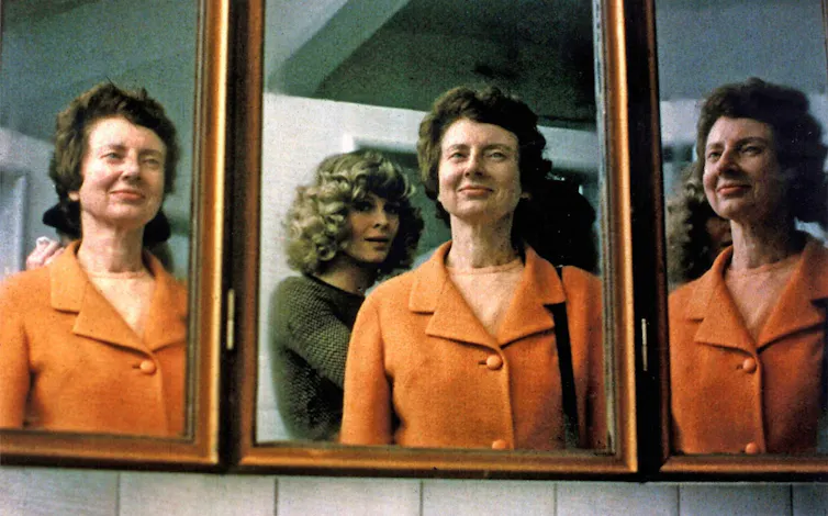 A mirror showing a blind woman from three angles, one with another woman talking to her.