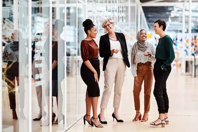 Un grupo de cuatro mujeres charla y se ríe de pie en los pasillos de una oficina.