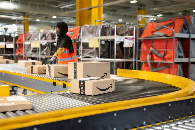 A worker sorts Amazon packages on a conveyor belt in a warehouse.