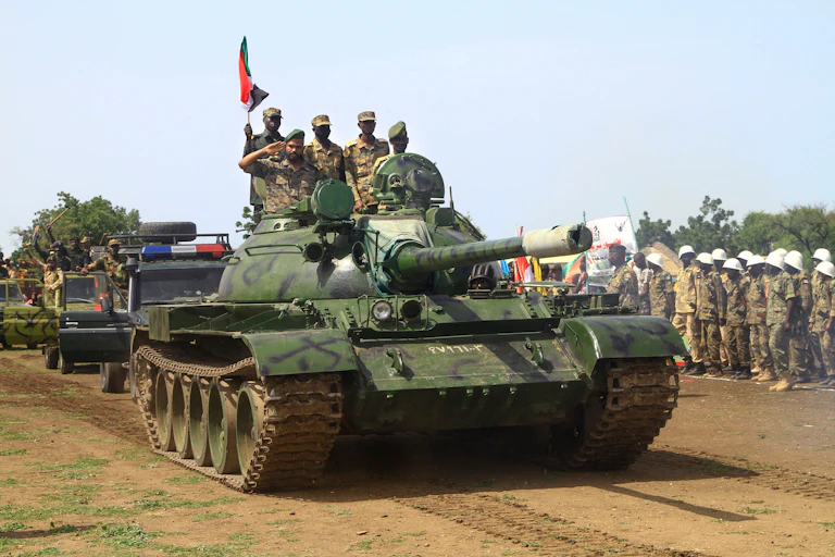 Military members ride tank down dirt street in procession