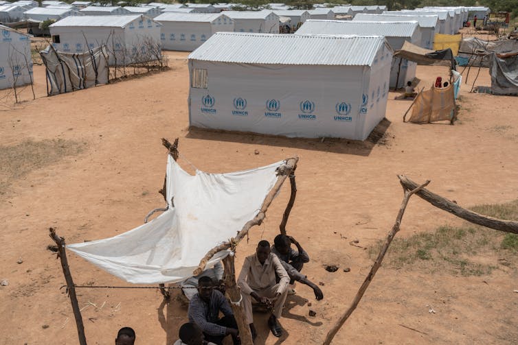 Small group of people sit in shade in a refugee camp