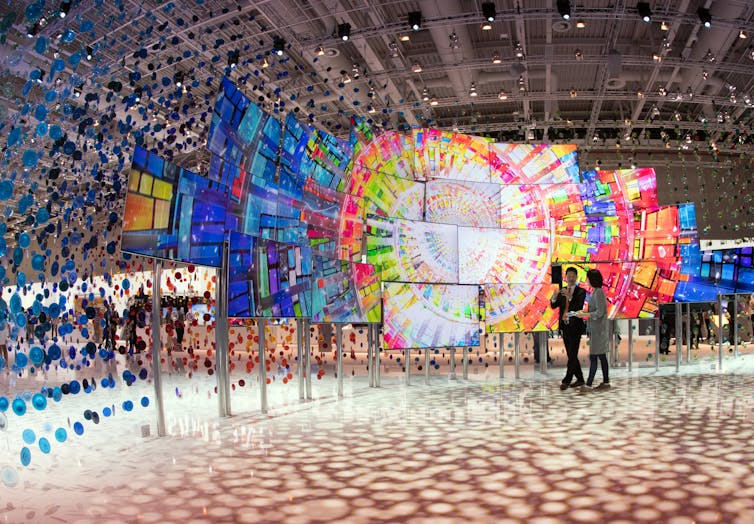 people walk past colorful multi-screen display at a trade show