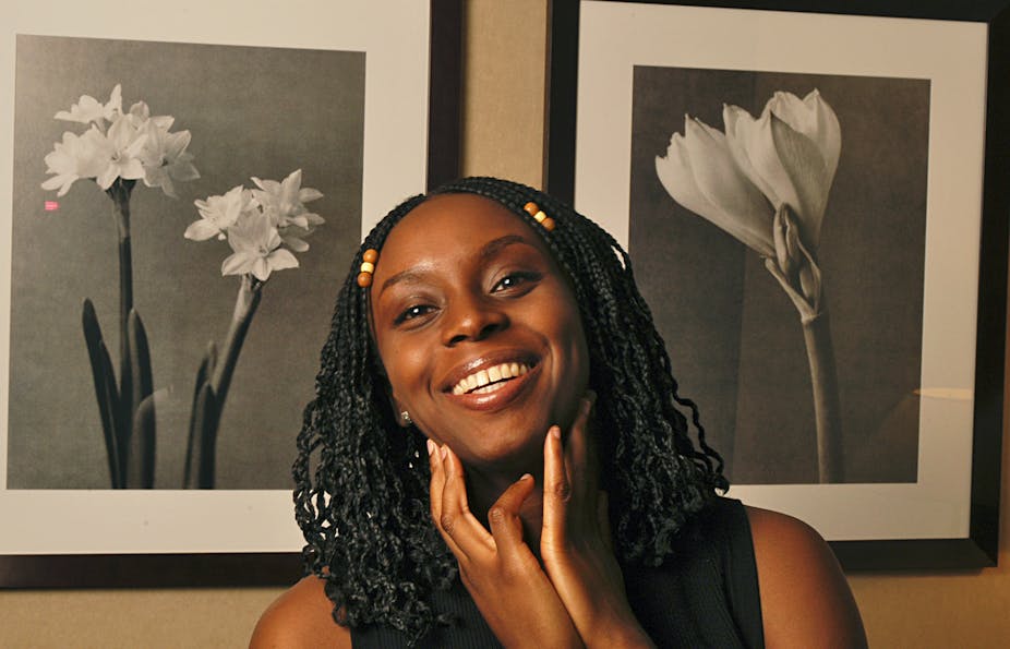 Dreadlocked woman smiling and posing in front of two black and white photographs of flowers.