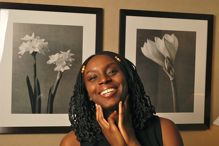 Dreadlocked woman smiling and posing in front of two black and white photographs of flowers.