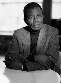 Black and white portrait of African man wearing a tweed coat sitting at a table.