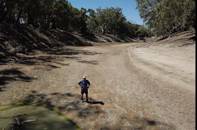 A farmer stands in a dry river bed