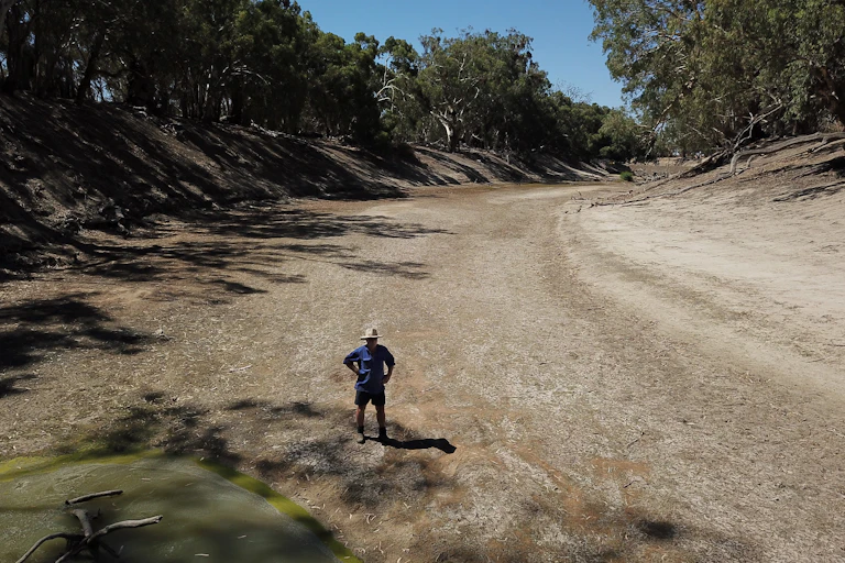 A farmer stands in a dry river bed