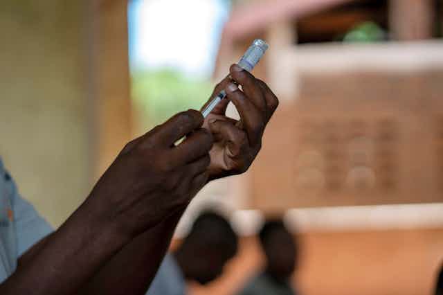 Hands drawing up a vial of malaria vaccine.