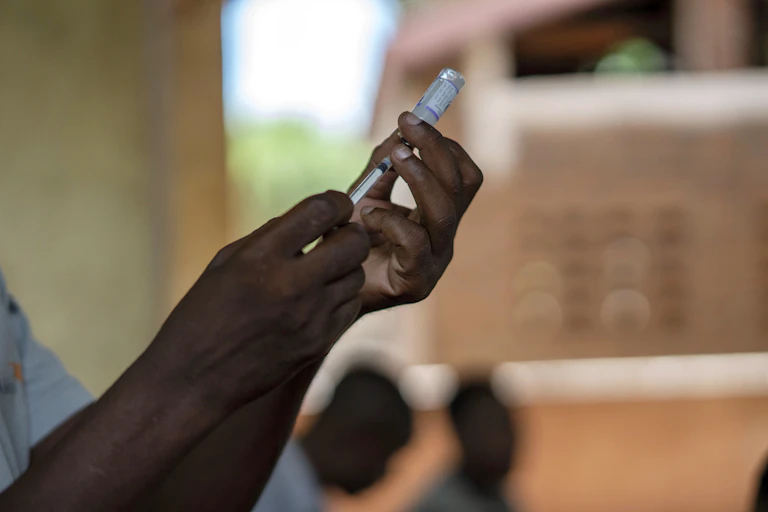 Hands drawing up a vial of malaria vaccine.