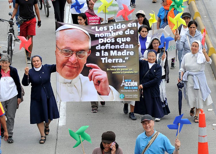A few Christian nuns and other women walk on a street during a march, holding a banner of Pope Francis.