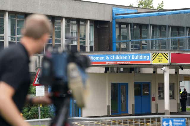 Camera operator (blurred) outside a building with the sign: Women & Children's Building.