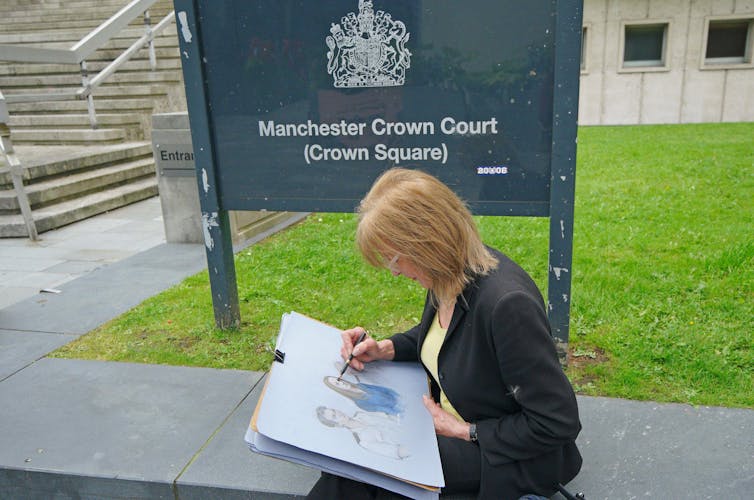 Woman with drawing pad sits on a wall in front of sign for Manchester Crown Court.