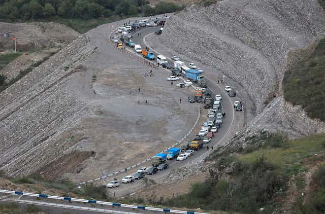 A convoy of cars along a winding highway amid gravelly hills.