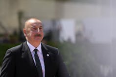 A bald man with a moustache wearing a dark suit.