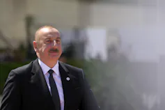 A bald man with a moustache wearing a dark suit.