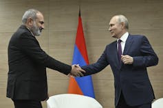 Two men in suits shake hands.