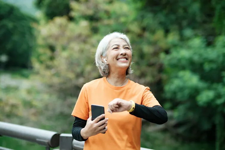 Femme aux cheveux gris en tenue de sport qui consulte son téléphone.