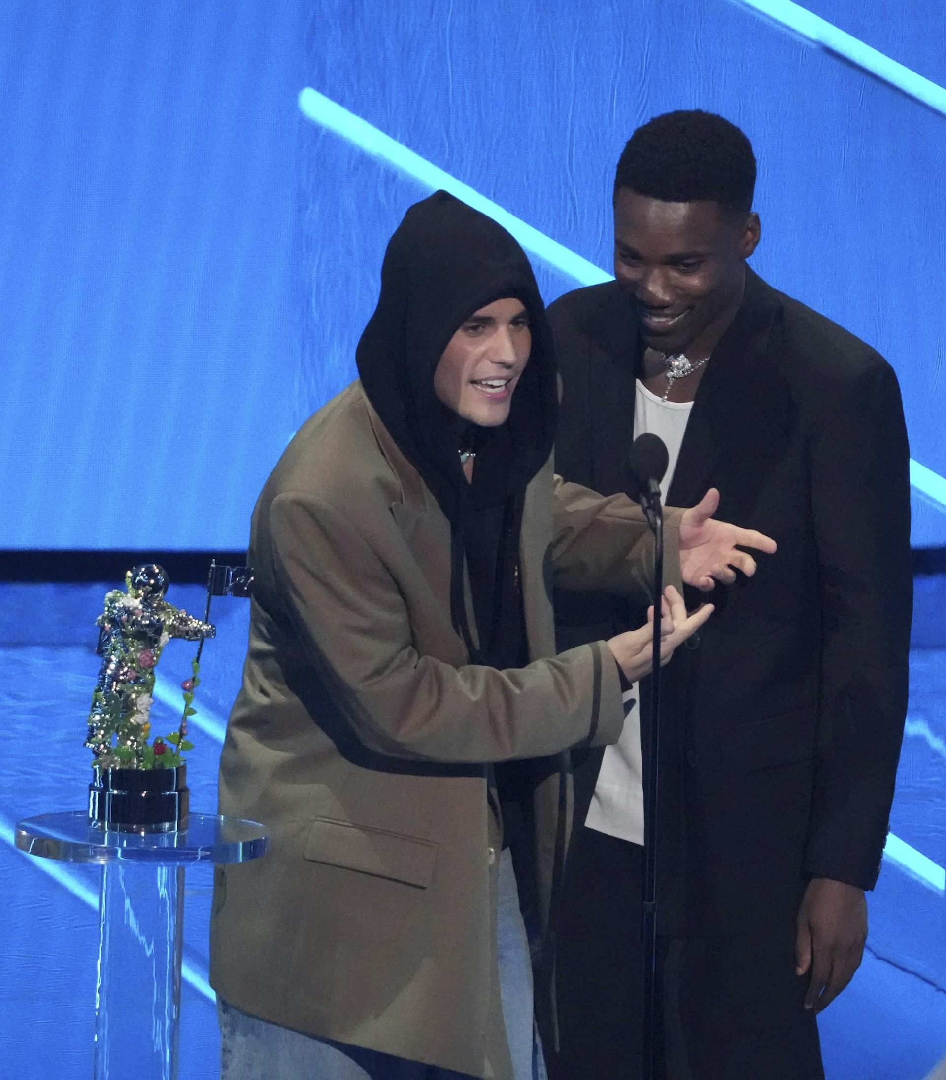 Two men stand before a microphone on a stage.