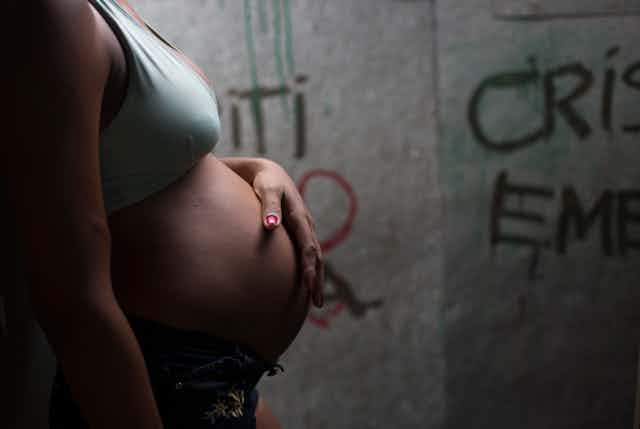 Mulher grávida, de perfil, em frente a uma parede pixada