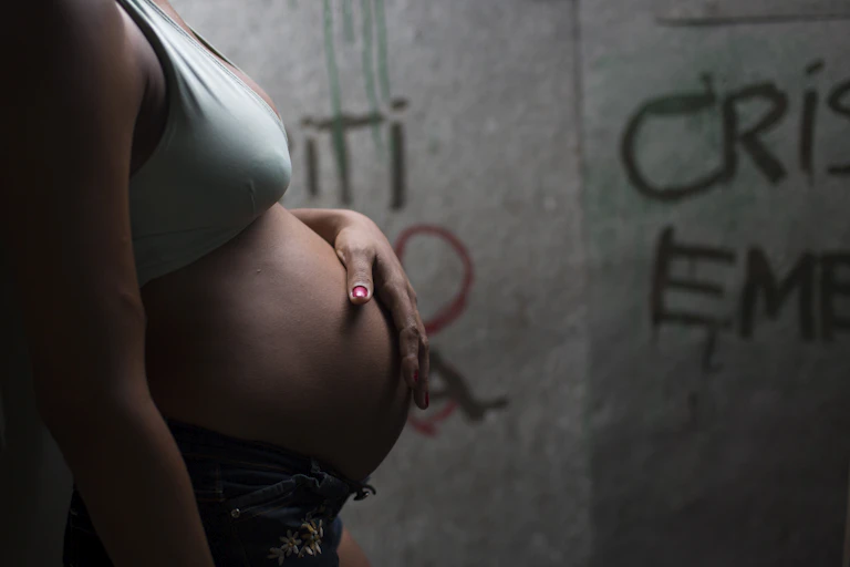 Mulher grávida, de perfil, em frente a uma parede pixada
