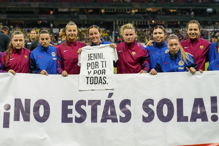 A group of women soccer player hold up signs in spanish