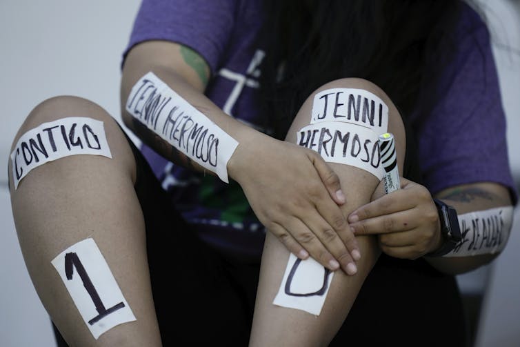 A woman places tape on her legs and arms that reads Jenni Hermoso 10