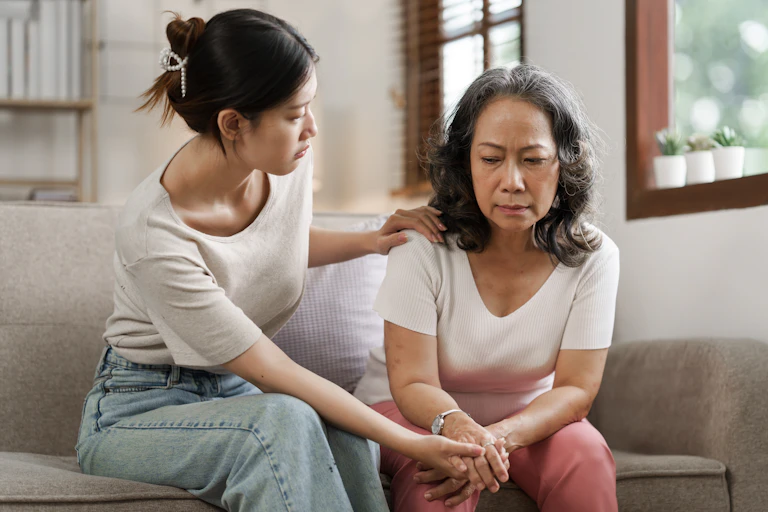 A younger woman looking concerned about an older woman sitting on a sofa