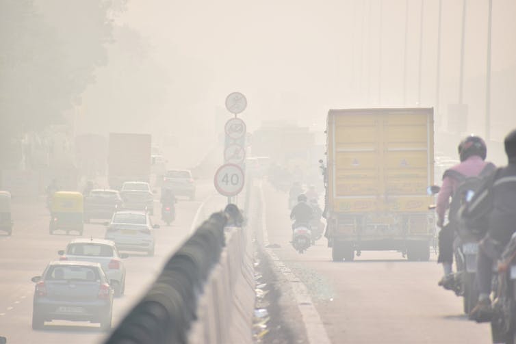 A smog shrouded road with motorcycles, trucks and cars barely visible through the pollution