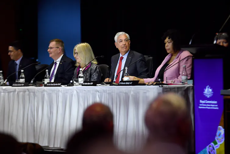 Several adults sit behind a long table on stage at formal event.