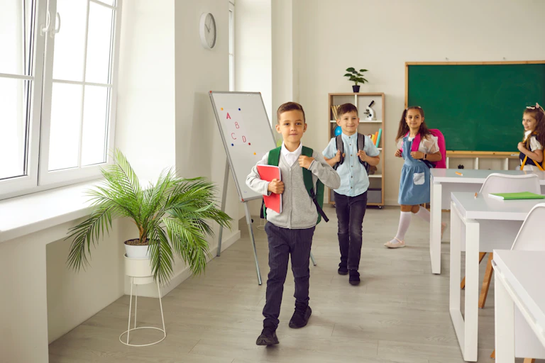Cuatro niños salen de clase con las mochilas puestas.