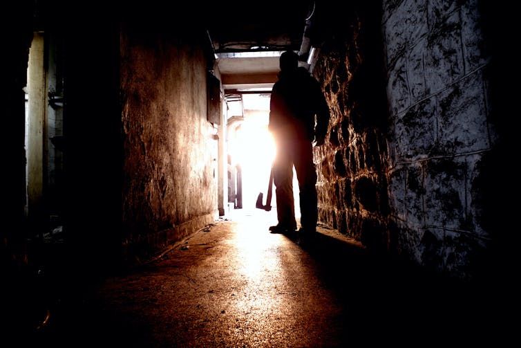 Silhouette of a man holding an axe in dark hallway.