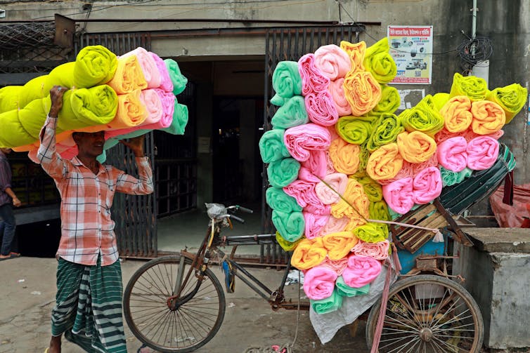 A man loading many colourful mosquito nets onto a bicycle