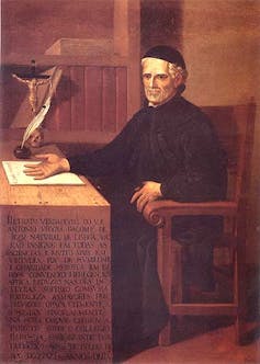 Pintura mostra um padre sentado numa mesa, com a mão sobre um papel que está na mesa, onde também se vê um crucifixo e uma pena para escrita