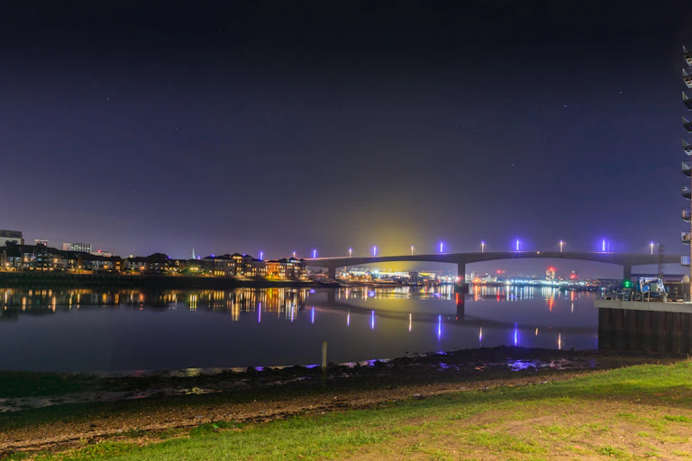 A bridge over a river is lit up at night.