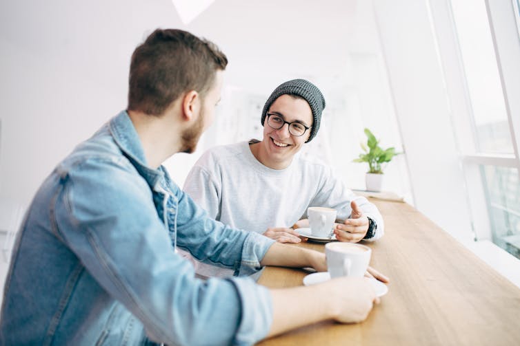 Two men sit at a table drinking coffee and talking