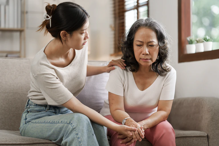 A younger woman looking concerned about an older woman sitting on a sofa