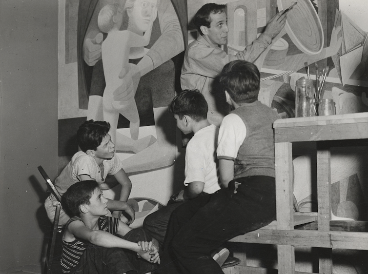 black and white photo of Philip Guston working on a mural with a group of children looking on.
